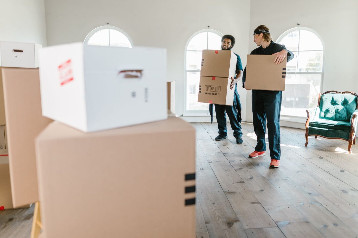 Two movers in uniform carrying boxes across a bright, empty room