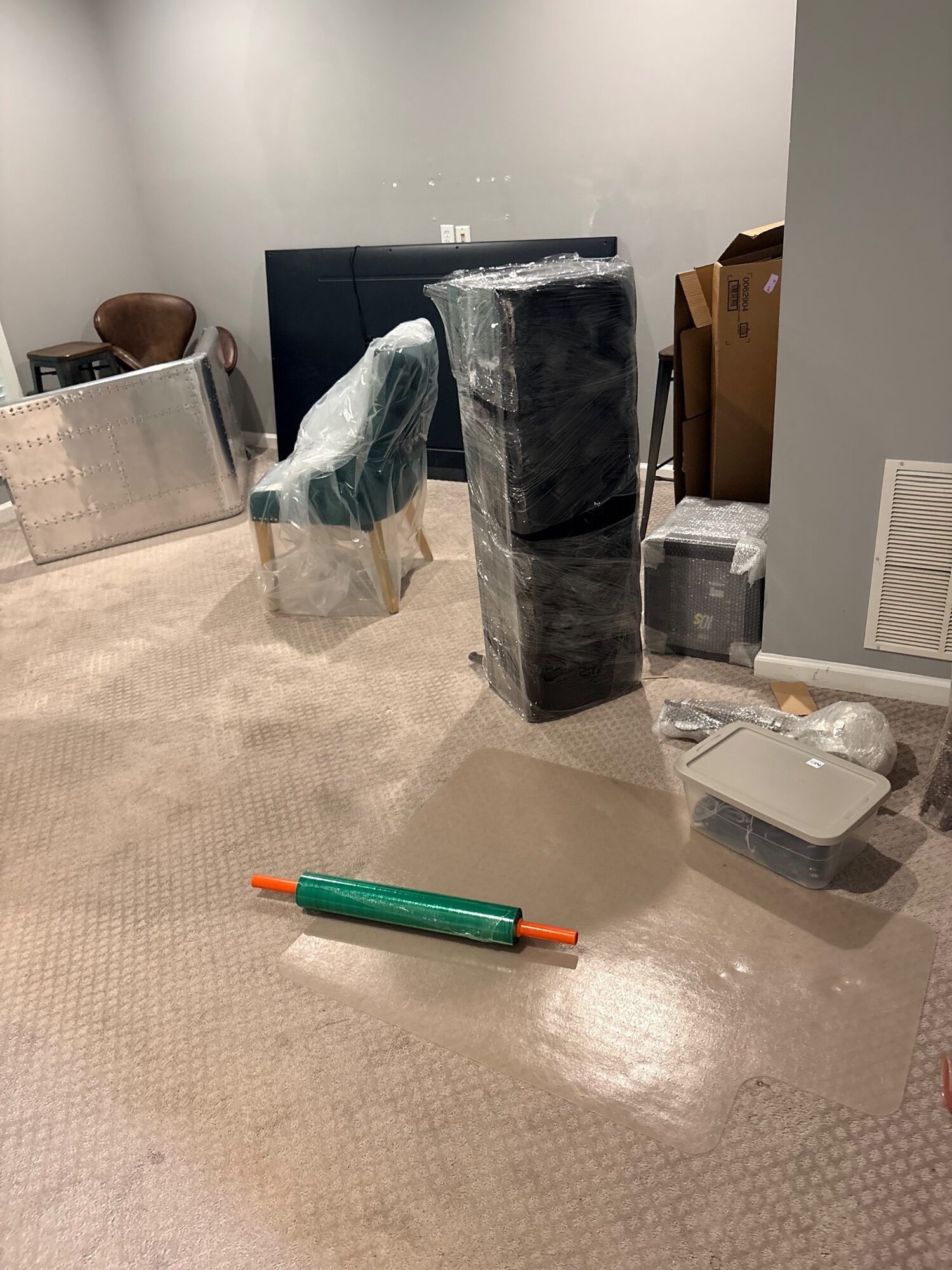Wrapped furniture stacked in an empty room with a roll of stretch film on the floor